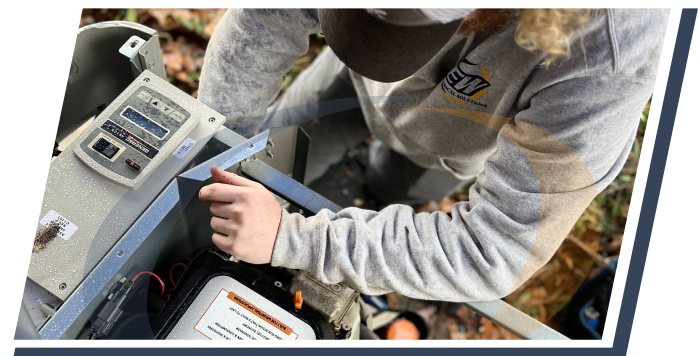 an electrician for e&w crouches down in the grass and leans an arm on the front of an open generator